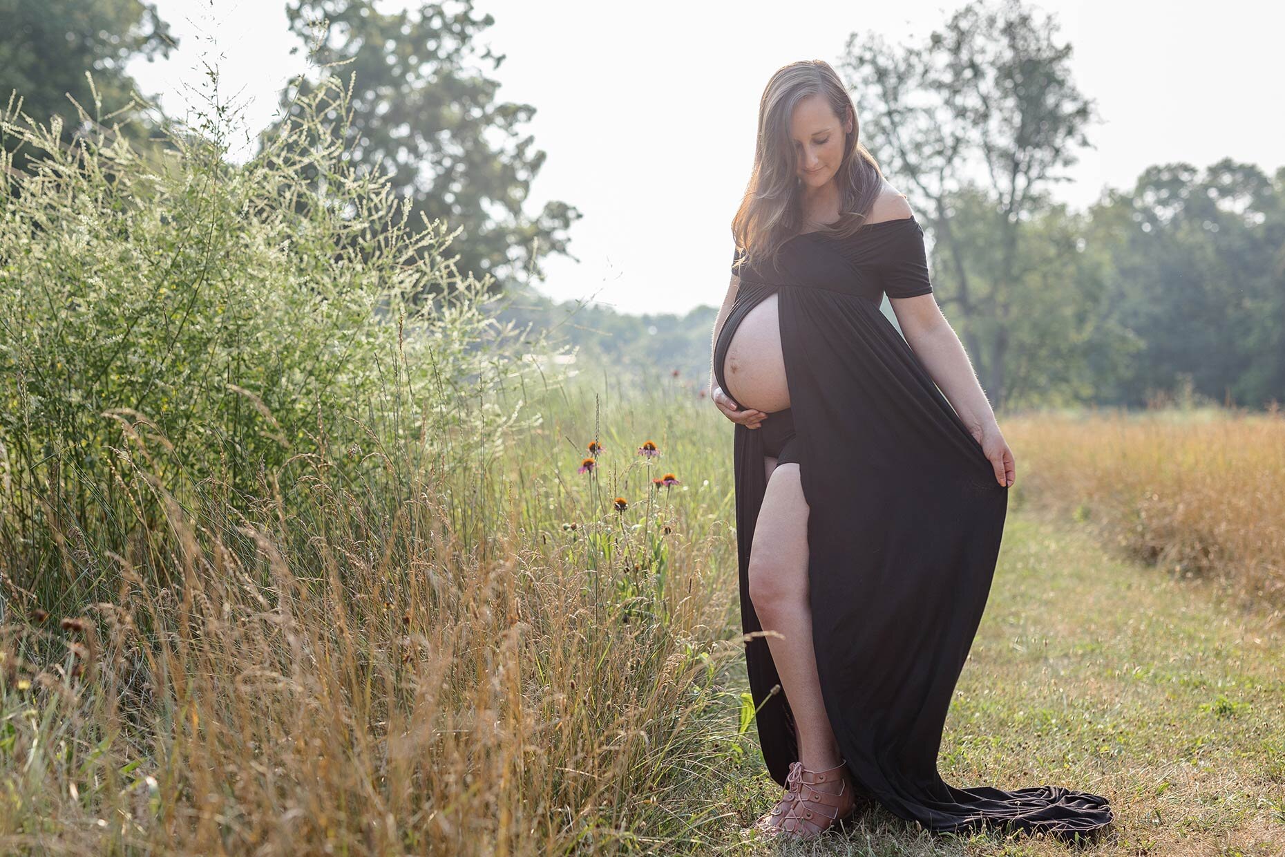 Maternity black dress with belly showing in flower field