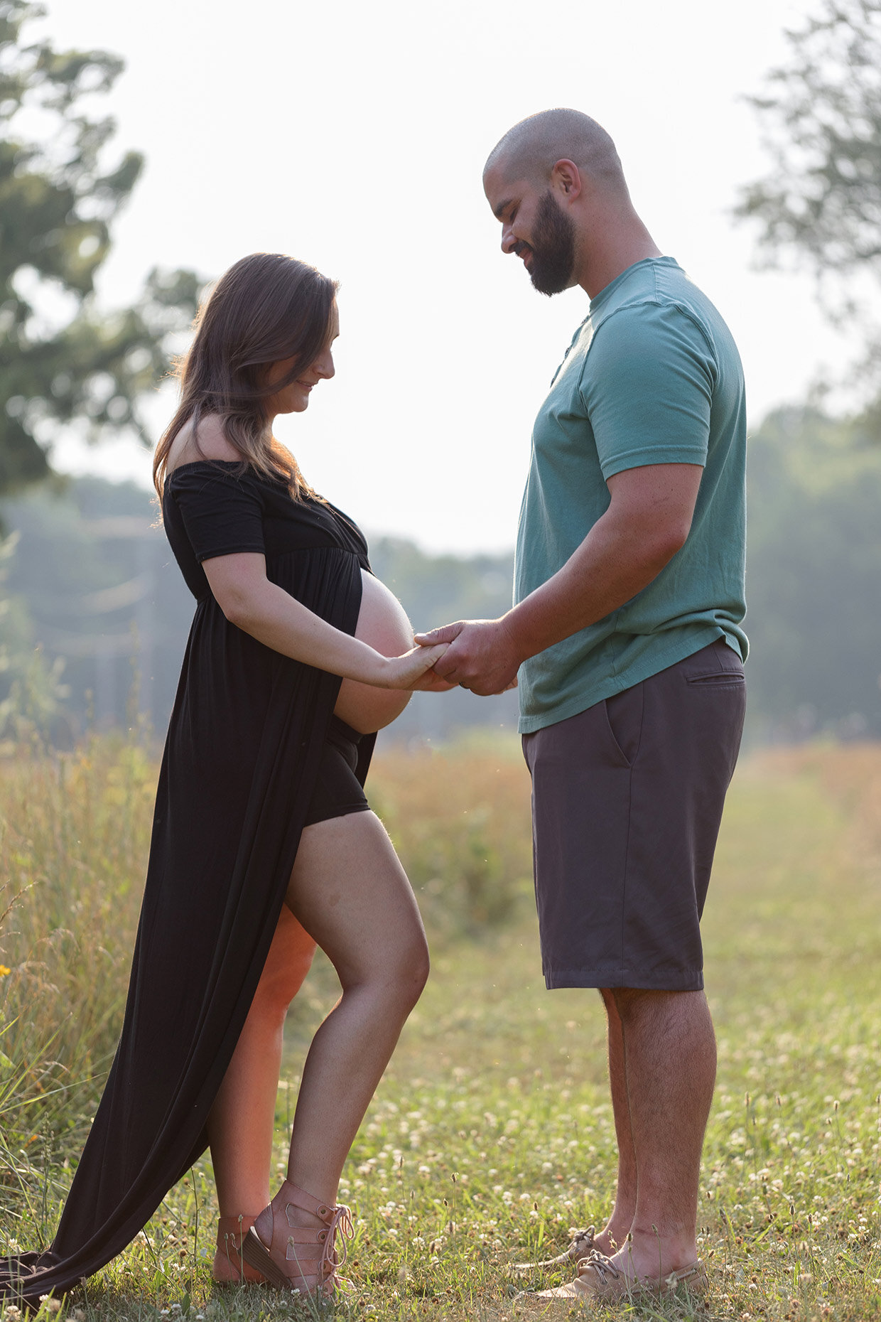 Maternity looking at bare belly in black dress in field during golden hour