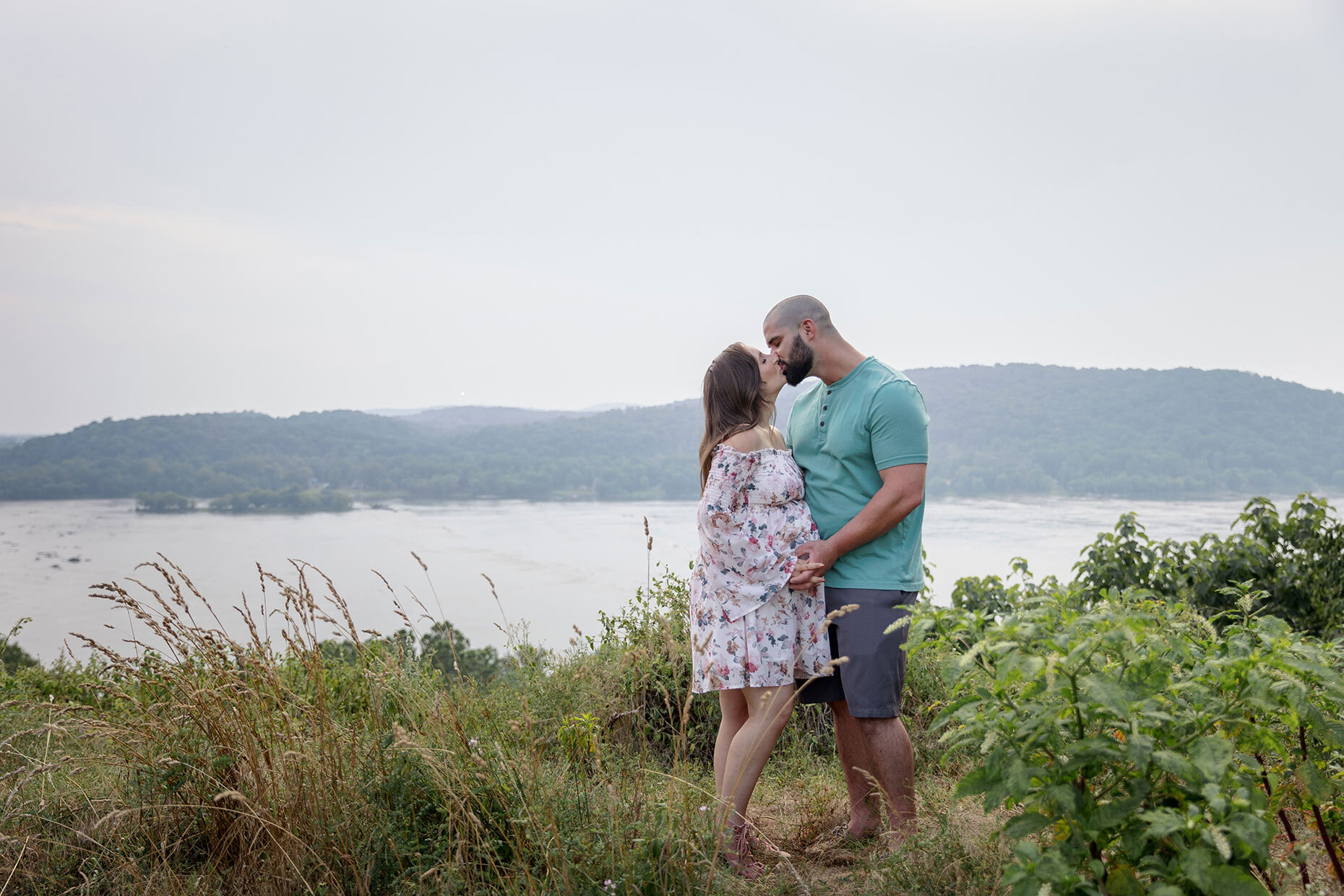 Maternity couple by River in grass overlook Kissing