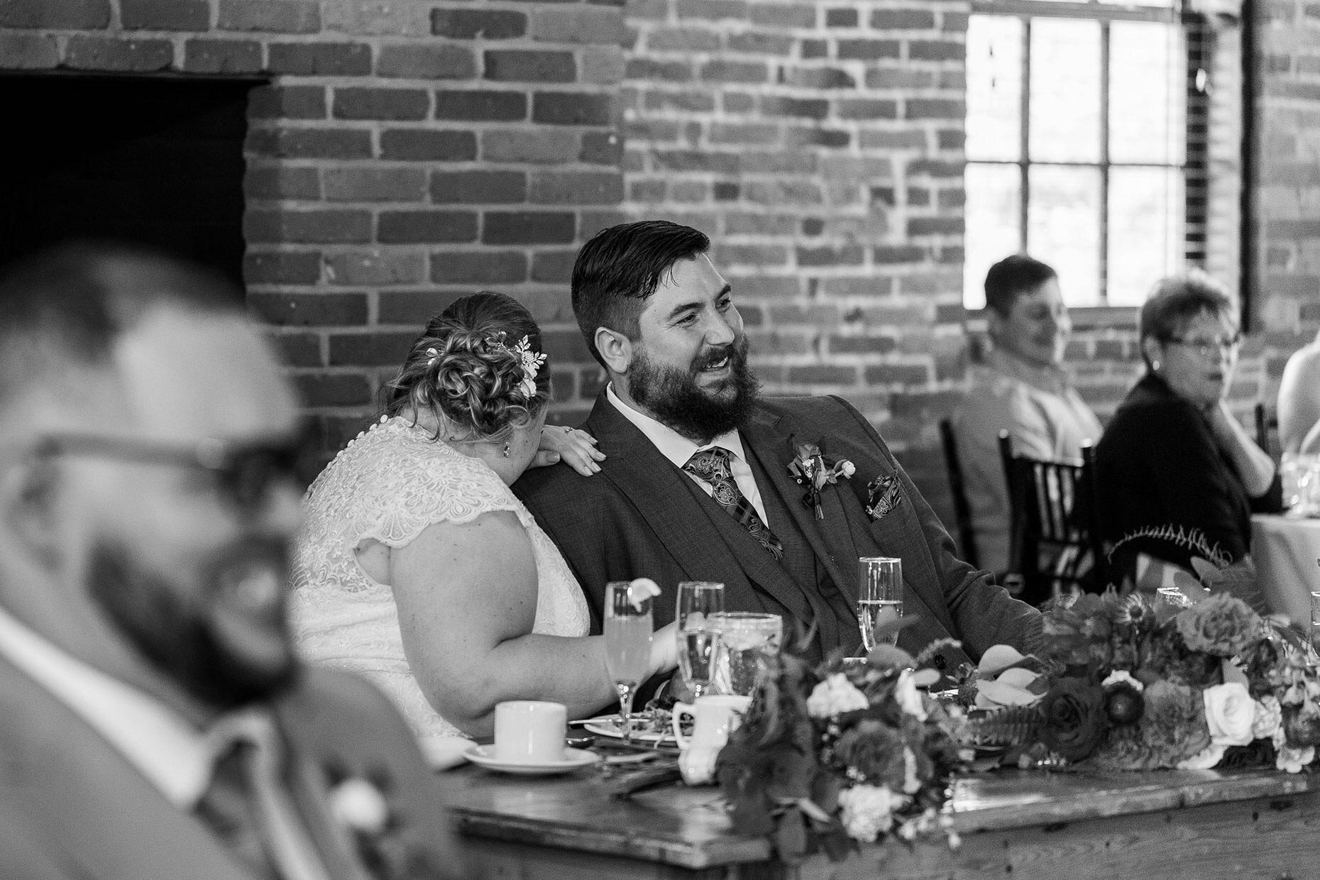 Bride and groom laugh at toasts in black and white