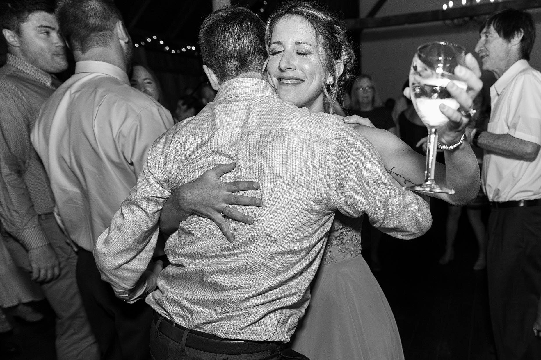 Bridesmaid dances with wine at reception, hugging