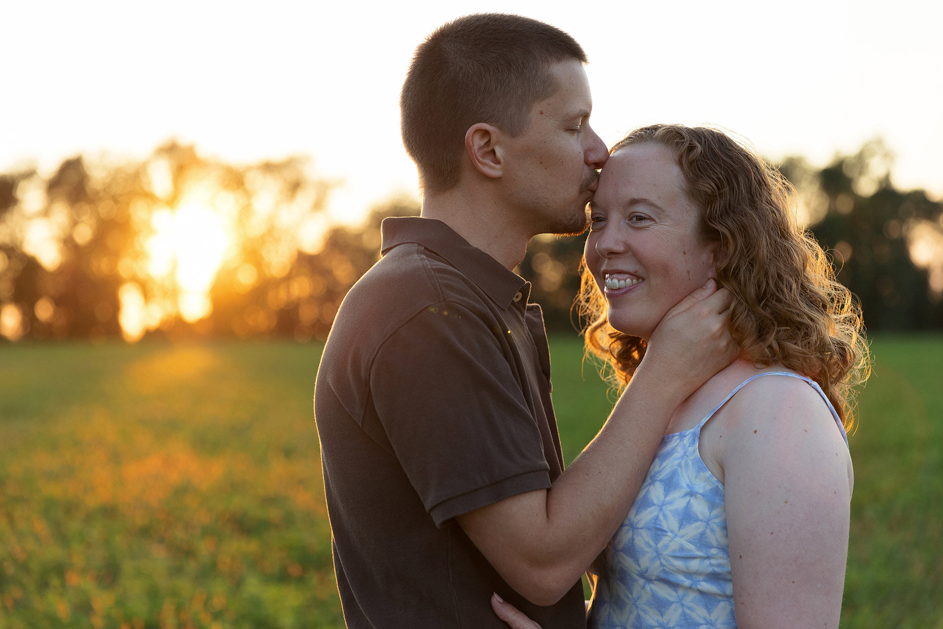 Couple kissing forehead at sunset in field 