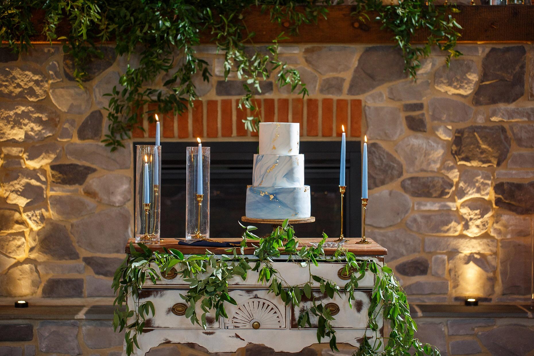Blue candles and three tier cake in front of stone fireplace
