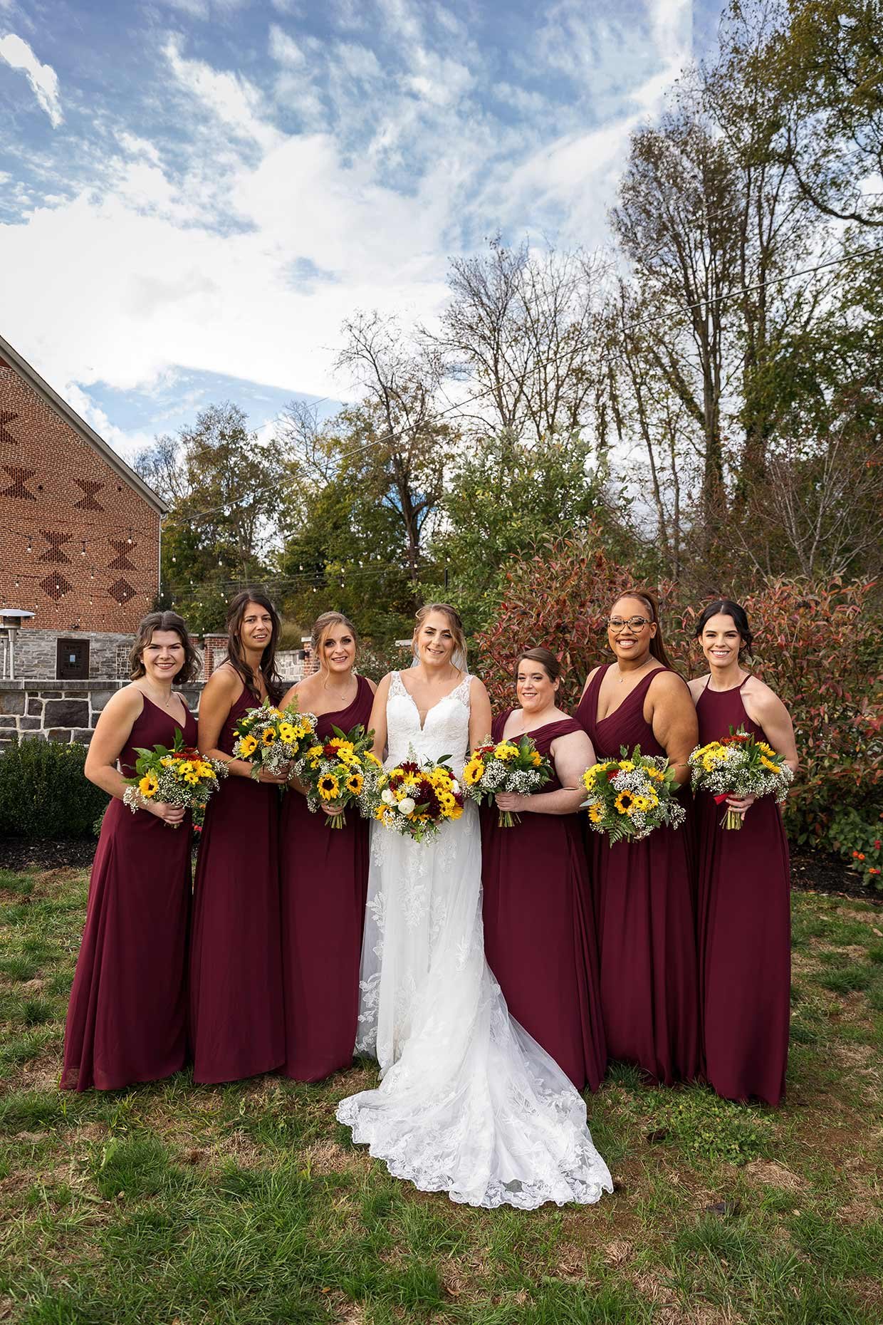 Bridesmaids in front of brick barn with blue sky