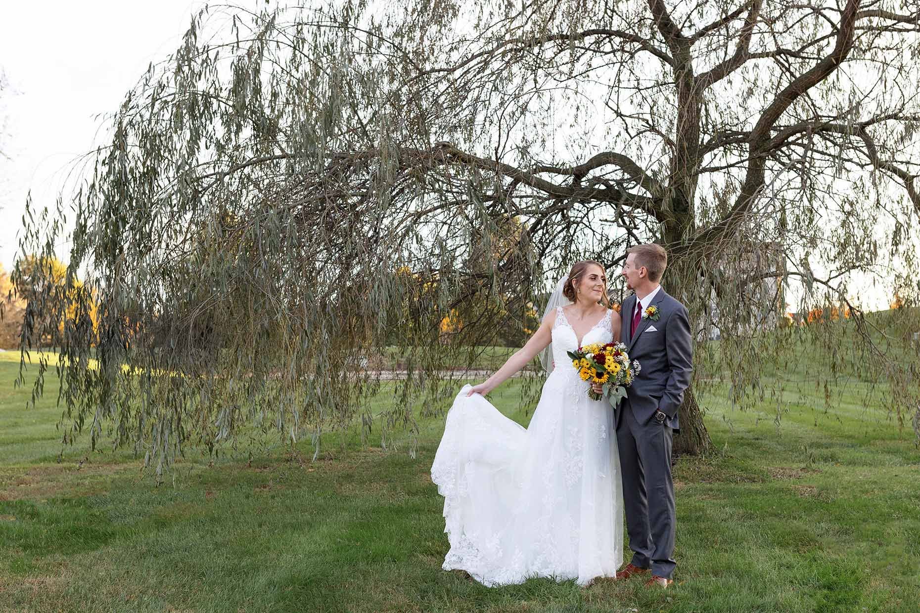 Bride holding train under a willow tree